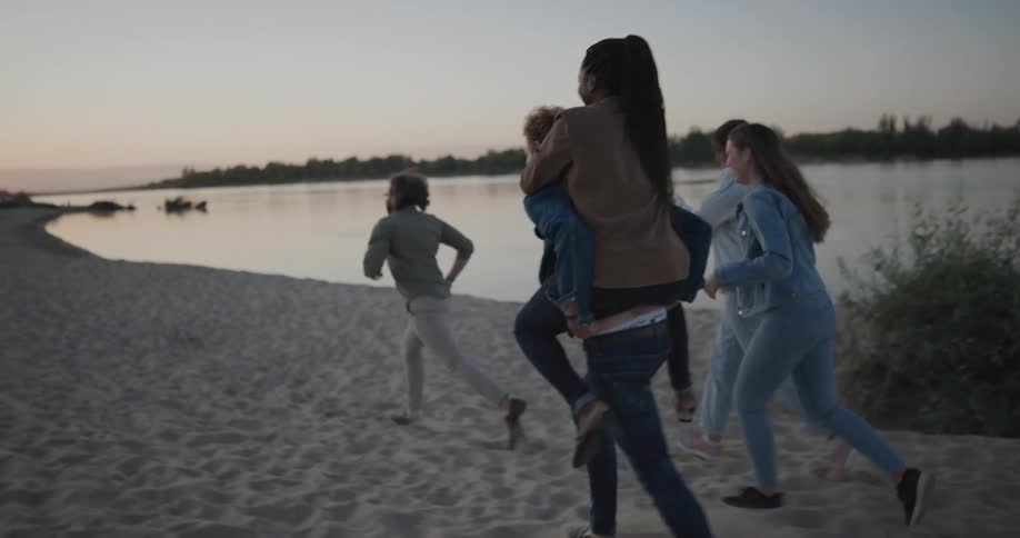 A group of friends run around a lakeside beach laughing together