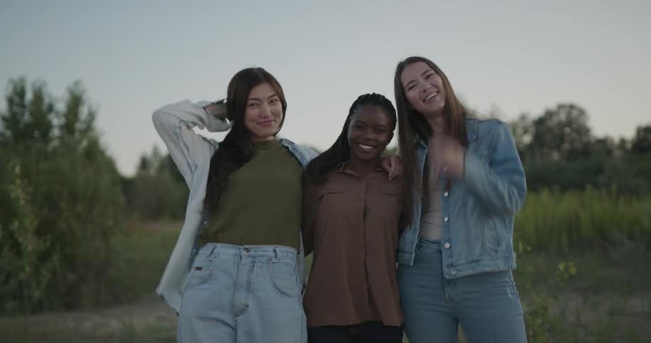 Three friends laugh and wrap their arms around each other while posing in a field