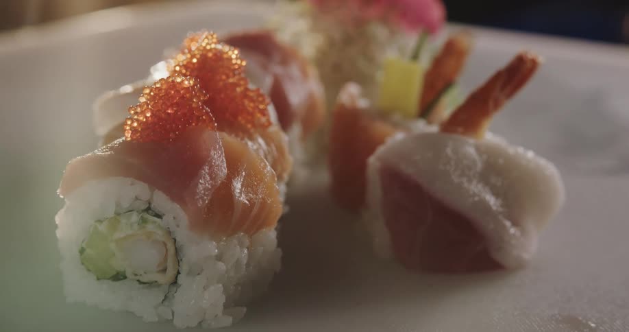 A person putting the final ingredient on top of a roll of sushi