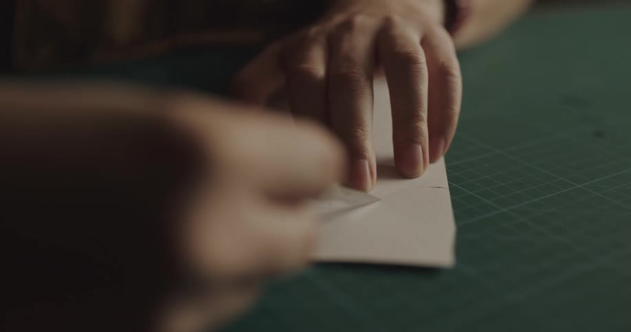 A person traces around their finger with a blade on paper and cuts as they trace