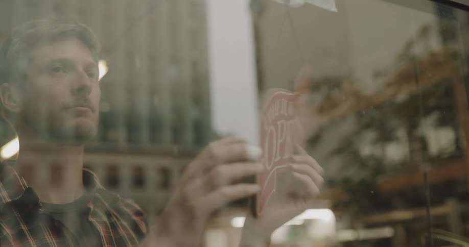 Business owner changing the open sign on the window of his business for closed sign