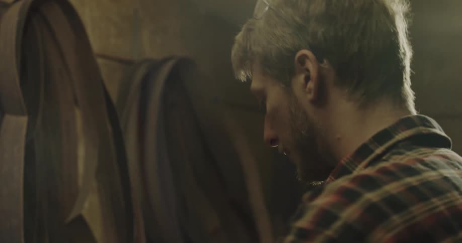 A man selects a sandpaper belt from several hanging in his workshop and loads the machine