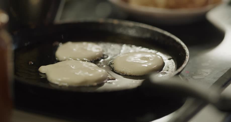 Mini pancakes cooking on a black skillet on a stove
