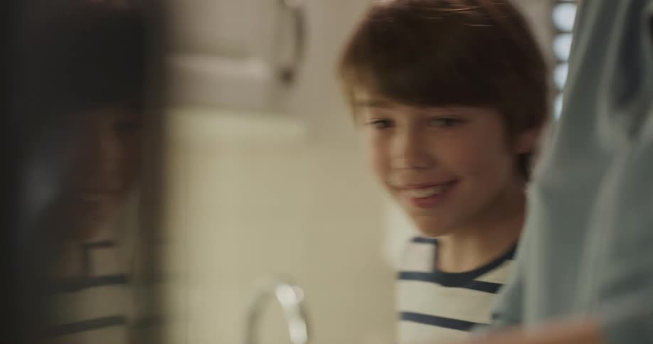 A boy and a woman in a kitchen with the woman hitting the boy on his hand