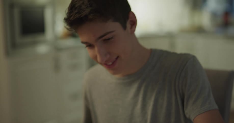 White teenager boy sitting on a table putting food on his plate to eat in a happy mood