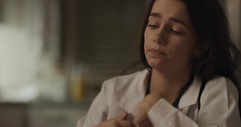 Female doctor putting down the grocery purchases at the kitchen taking off her mask stethoscope and sitting down in a sad mood