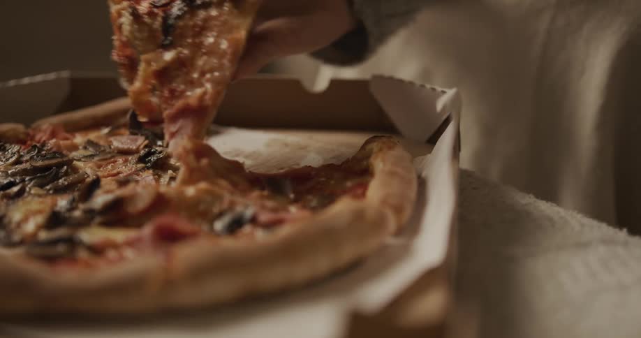 A person grabbing a piece of pizza out of a box