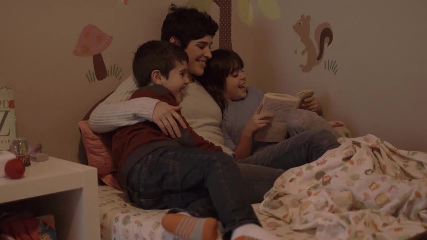 A child gets in bed with his mom and another child to read a book