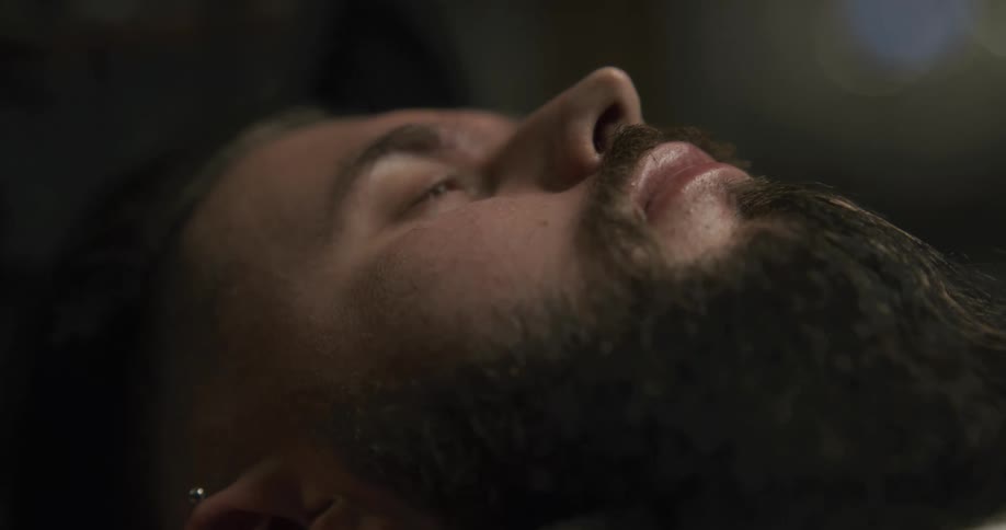 A barber removes a steamed towel from a mans face to prepare for a shave