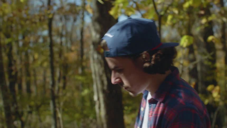 A man with a hat walking in a forest with trees the sky and clouds in the background