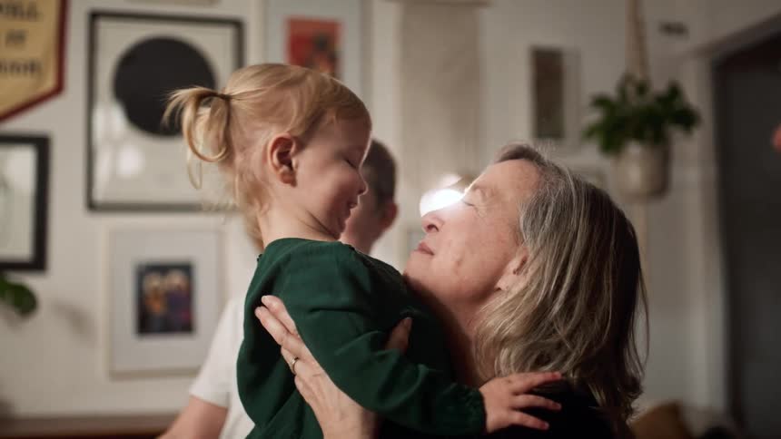 A woman smiles as she takes her grand daughter in to her arms as a young boy and elderly man watch