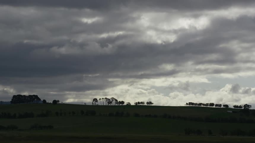 Clouds and darker clouds moving over trees and grass area