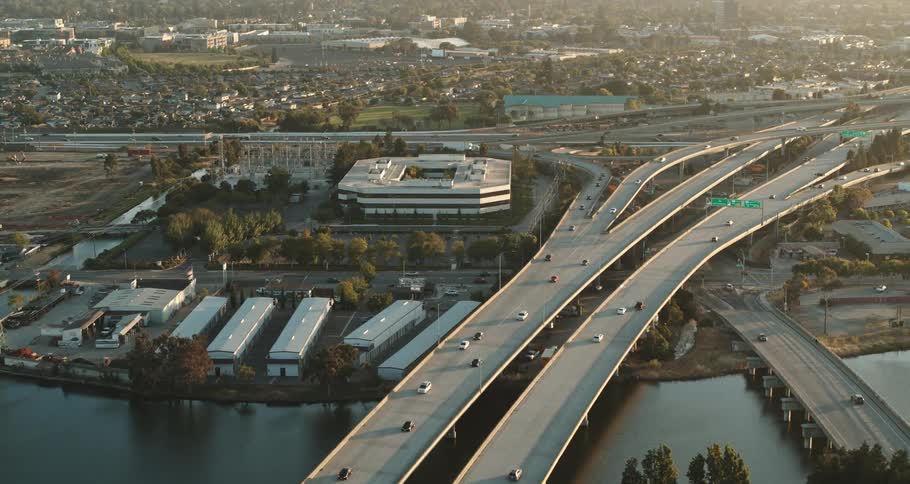 A highway with vehicles with bridges over a river with buildings and trees