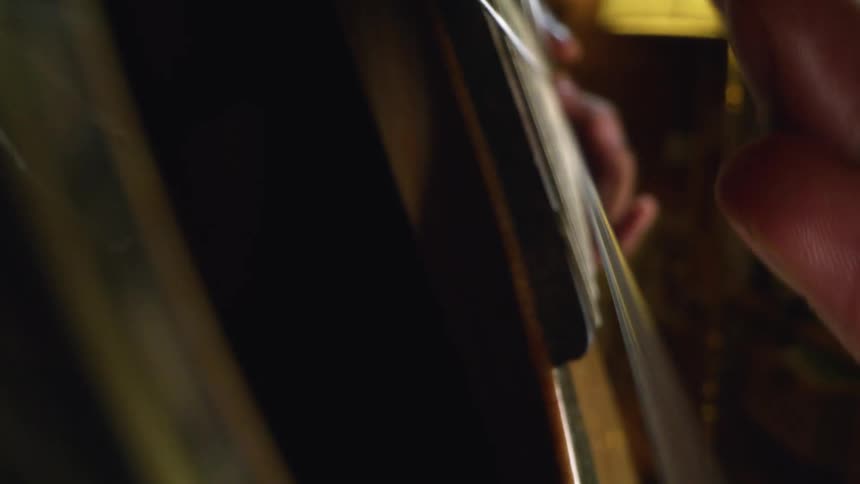 Person is playing an acoustic guitar and strumming the strings with their fingers