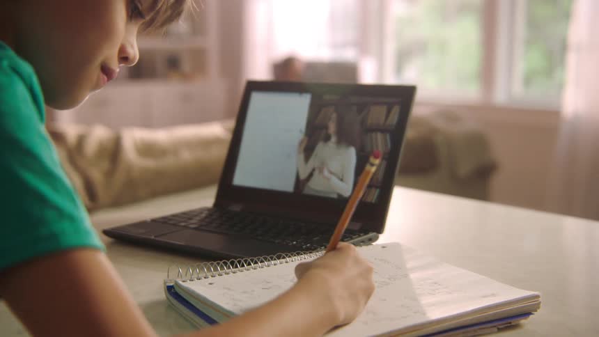 A boy is writing in his notebook during an online class