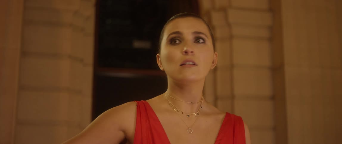 A woman in a red dress approaches the camera and stops to search her surroundings before hurriedly descending out of frame
