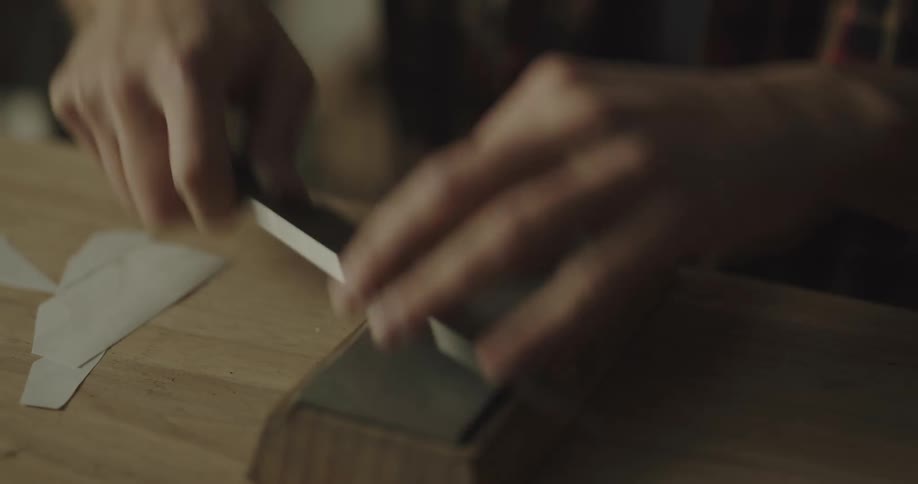 A man is using a whetstone on a wooden table to sharpen a chefs knife