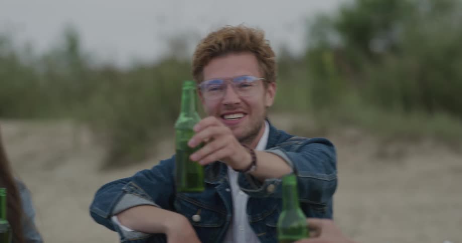 People sitting in a beach drinking beer from bottles with the sky and clouds in the background