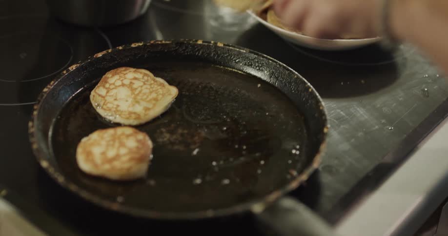 A person cooking pancakes in a frying pan and using two forks to place it in a bowl
