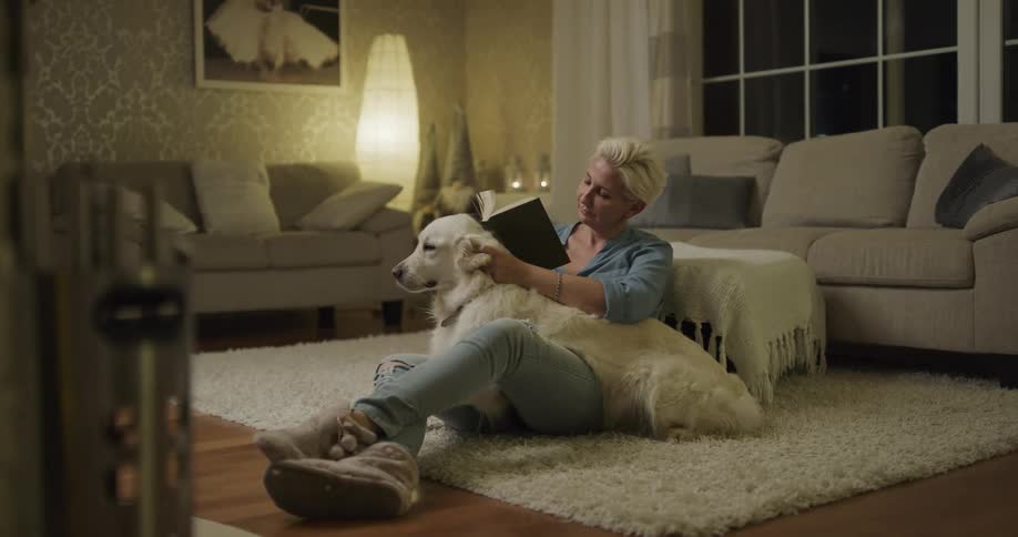A woman sitting around with her dog reading