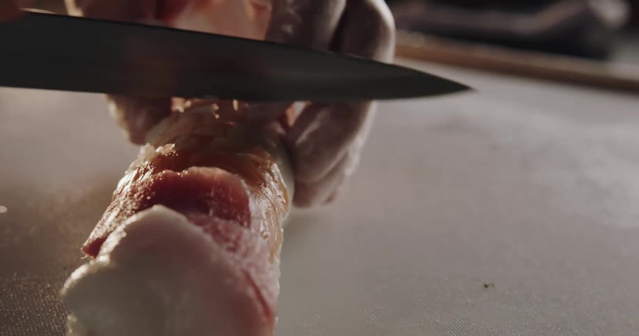 Man wearing disposable glove cutting off japanese food with a knife