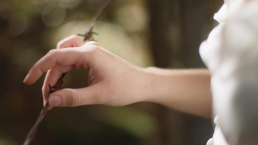 Females hand is holding barbed wire stretched across in front of her