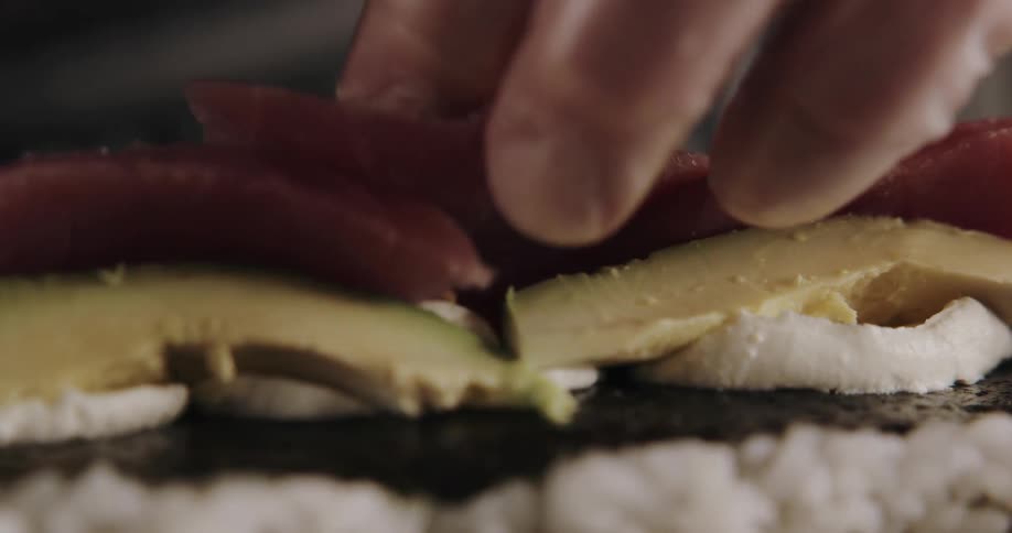 A man is rolling sushi while wearing gloves