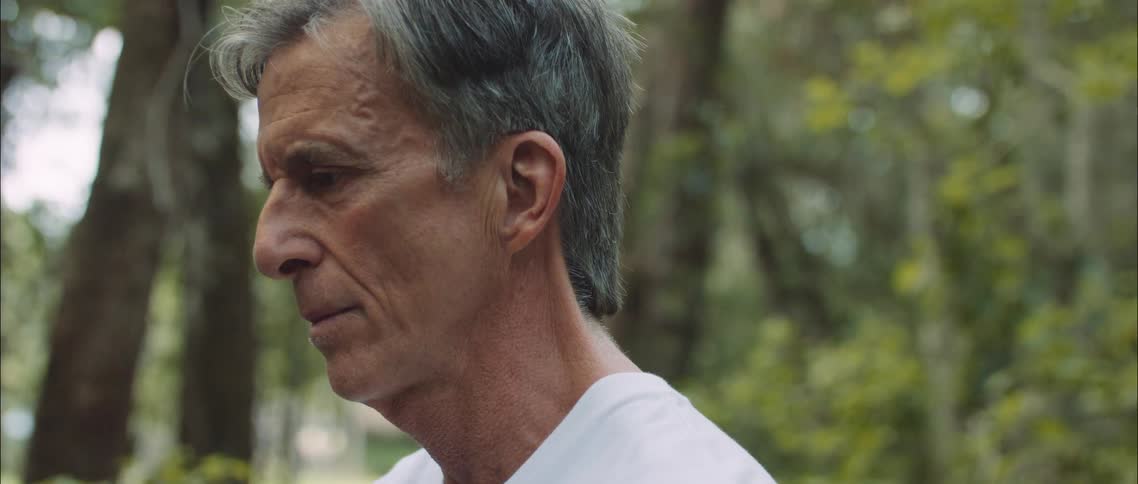 White old man sitting alone at a park with a contemplative and sad facial expression