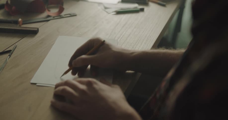 A man sits at a desk and sketches