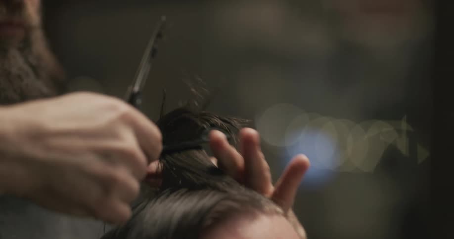 Bearded barber cutting the hair of a customer at the barber shop