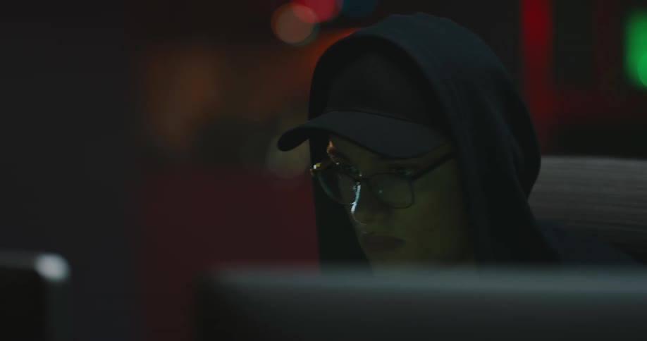 A teenage boy sits in front of a computer in a dark room