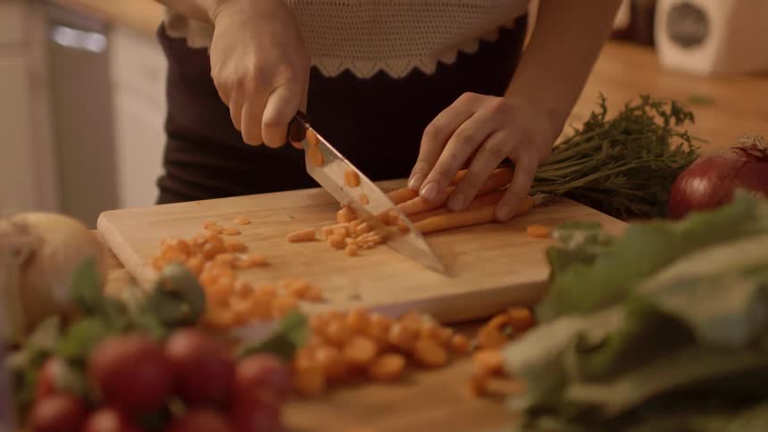 A woman dices carrots on a cutting board