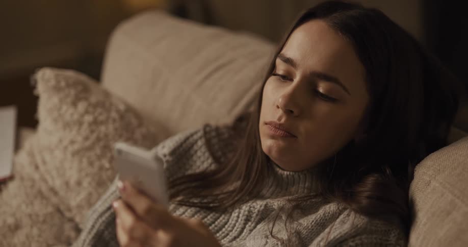 Woman lying back against pillows eats pizza while scrolling on mobile phone