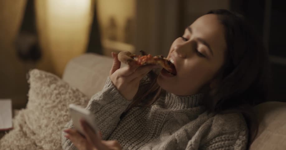 A woman eating pizza and using her phone
