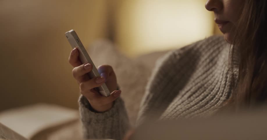 White teenager girl sitting at the couch using her smartphone while drinking coffee