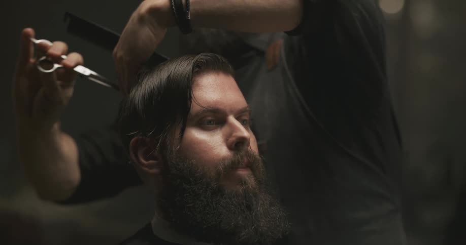 A man in a barbershop cutting another mans hair with a comb and scissors