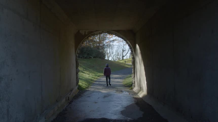 A man walks through a tunnel in a park and stops and turns as he reaches the end