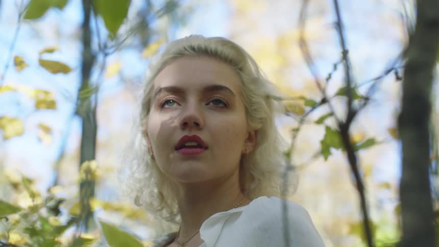 Blonde woman stands outdoors in woods on sunny day