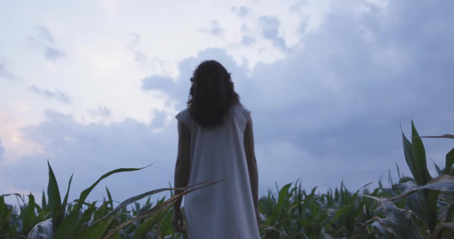 White woman wearing a white dress walking in the middle of the tall grass and turning around
