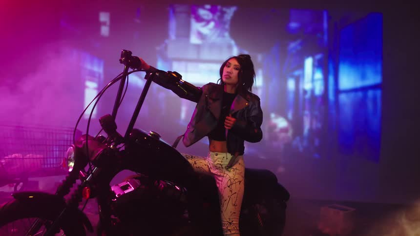 A woman poses on a motorcycle as lights flash and smoke billows