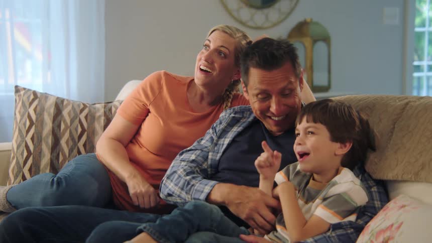 Family sitting together at the sofa watching tv and laughing
