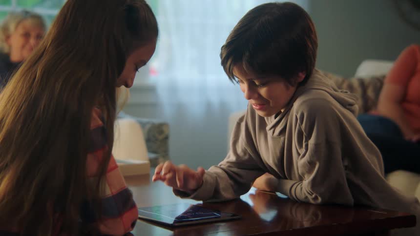Family sitting in living room watches kids play game on tablet