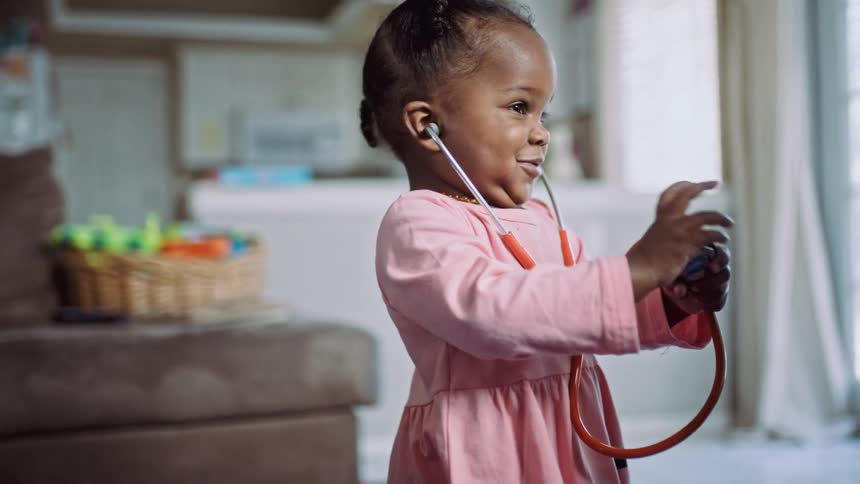 A little girl in a room with a stethoscope in her ear and walking up to a man and putting it on his head