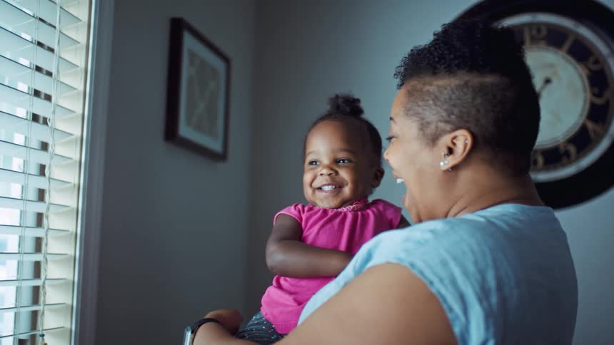 Black woman holding her daughter and pointing at the window while both laugh