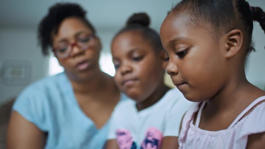 A little girl reads a book to her sister and mother