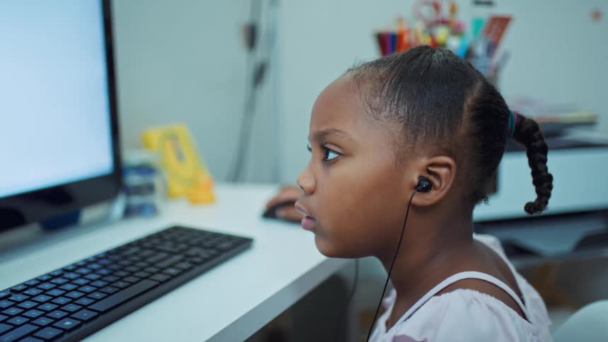 A girl sitting at a desk in front of a keyboard and computer