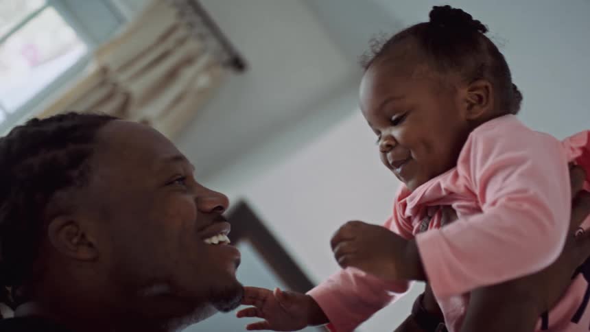 Black man lifts his young daughter into the air and they smile at each other