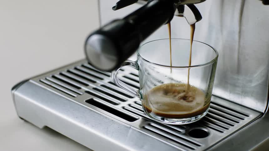 A clear glass coffee cup being filled on an espresso machine
