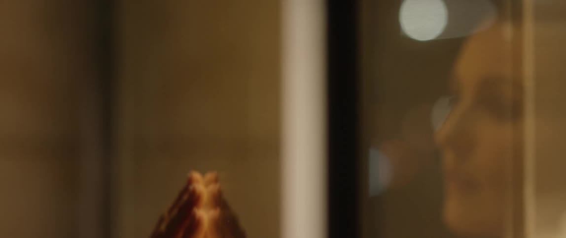 A woman looking in the mirror runs her hand down the mirror and turns away