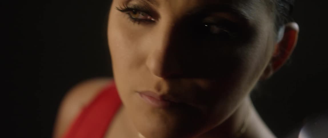 A dim light shines across the face of a brunette woman with her hair pulled back